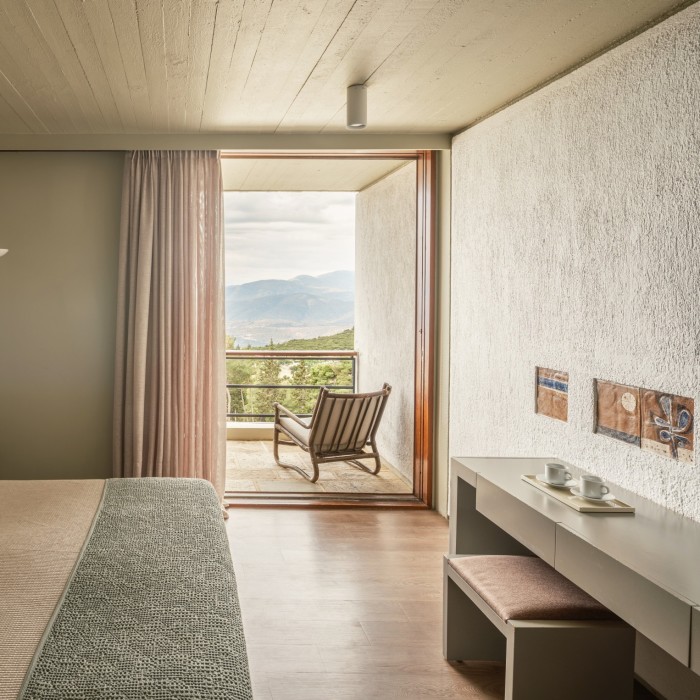 Inside a hotel room, with floor-to-ceiling windows leading out to a balcony which has a deck chair on it